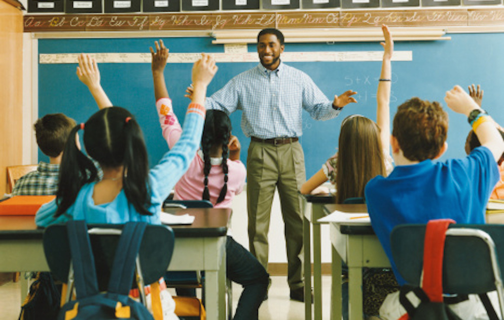 Teacher standing in front of classroom full of small children sitting at desks