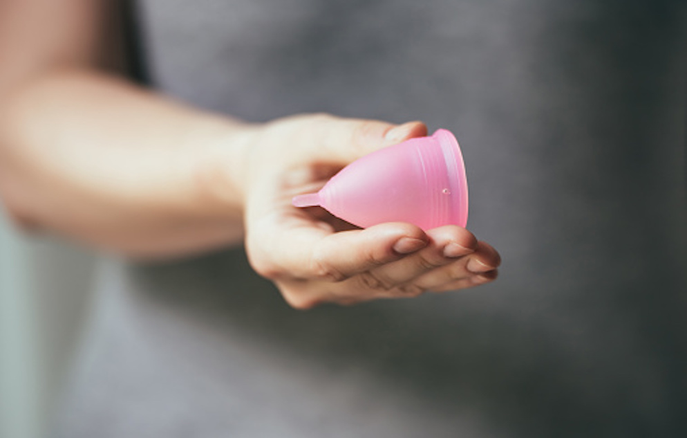 Image of a woman's hand holding a pink menstrual cup.