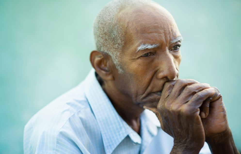 Photo of old African American man with his chin resting on his folded hands and thumb
