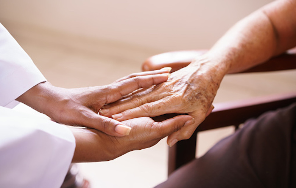 A caregiver's hands holding the hands of an elderly person.