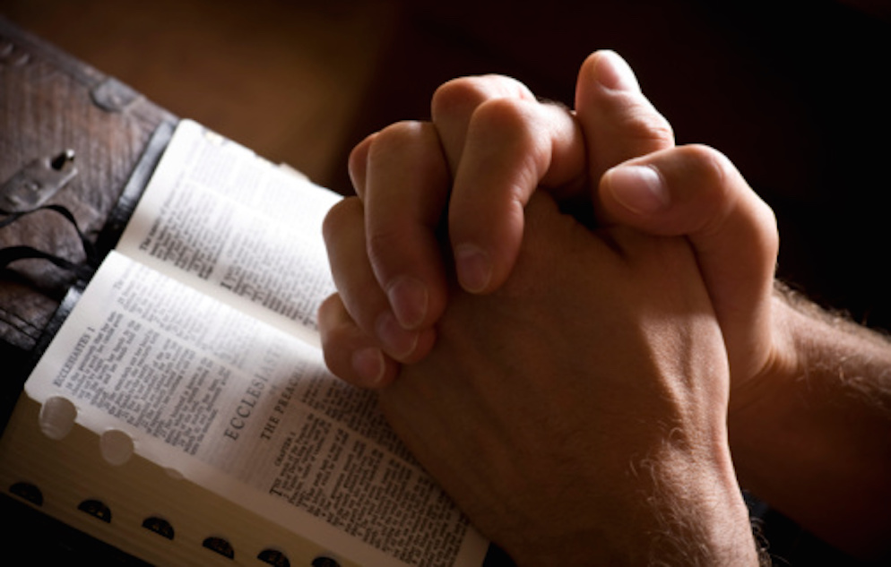 Praying hands on an open bible