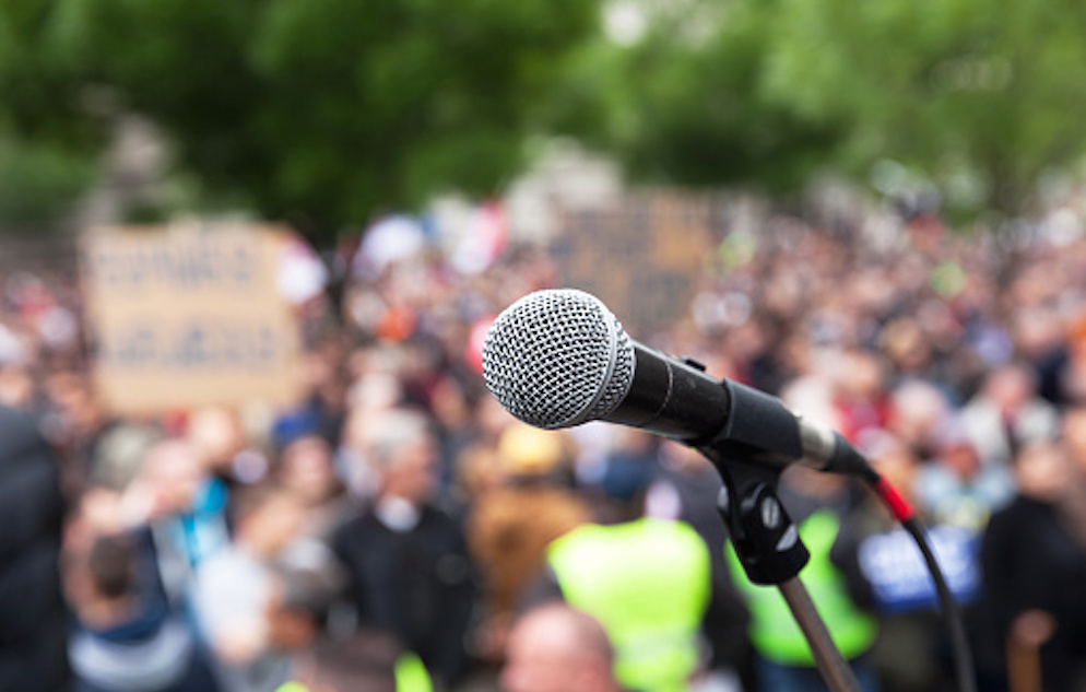 Close up and clear image of a microphone with a crowd of people in the background. The crowd in the background is out of focus.