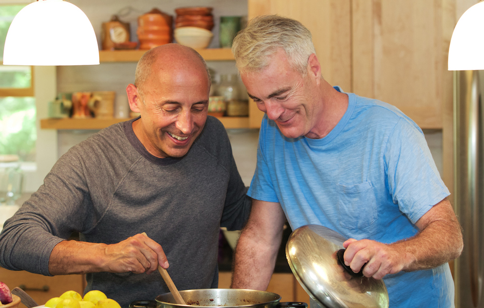 Senior gay male couple at home cooking together and smiling