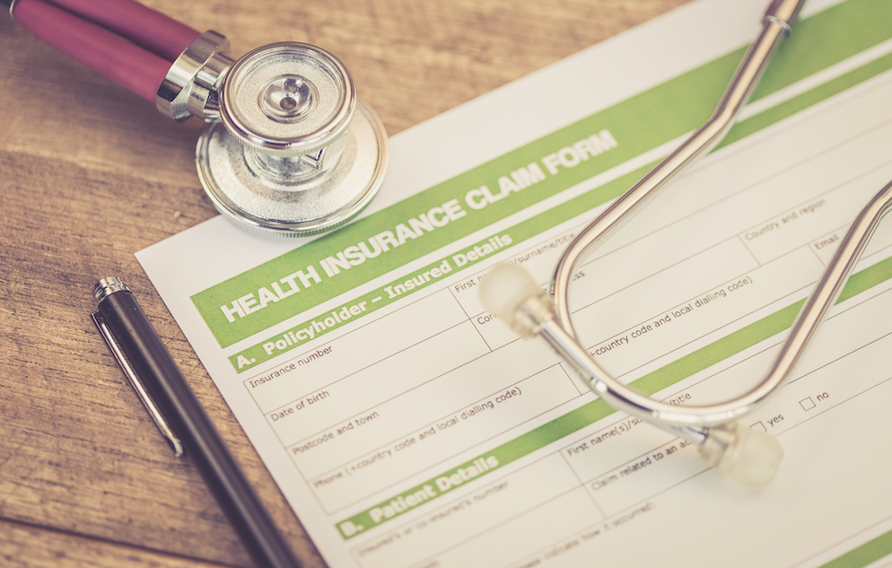 Close up of the upper left corner of a medical insurance claim form beside a pen and overlayed with the earpeice and chestpiece of a stethoscope.