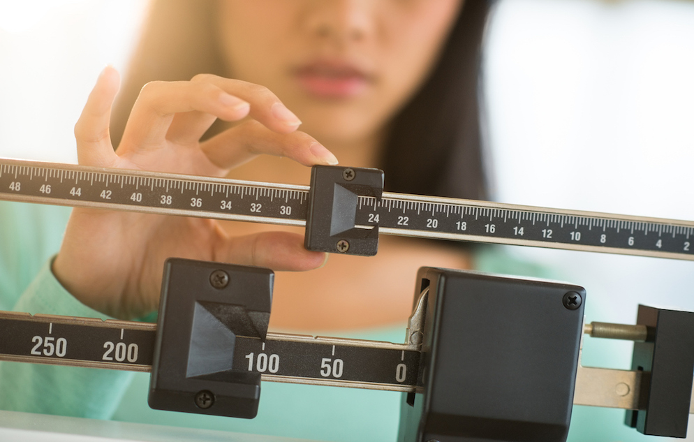 Adult woman with dark hair adjusting the balance of a weight scale