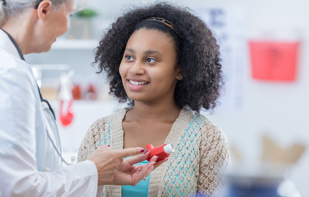 Confident senior female doctor teaches an African American teenage girl how to use an inhaler for asthma.