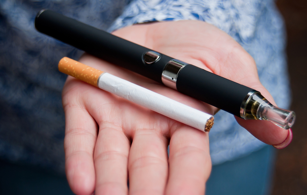 hand with e-cigarette and regular cigarette on it