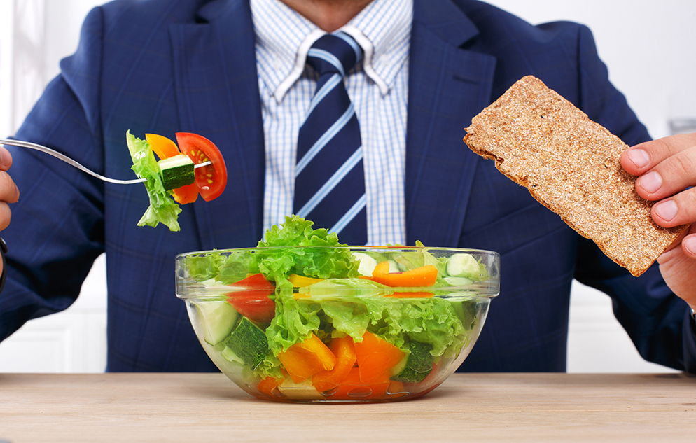 man in a suit eats a salad at a desk