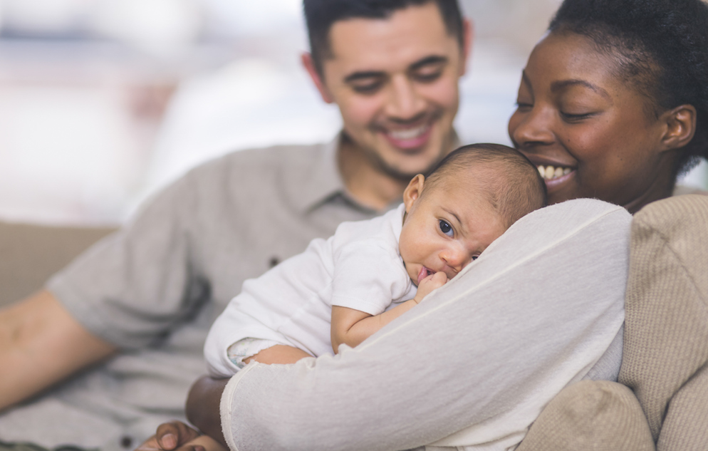 mother holds baby in arms while father looks on