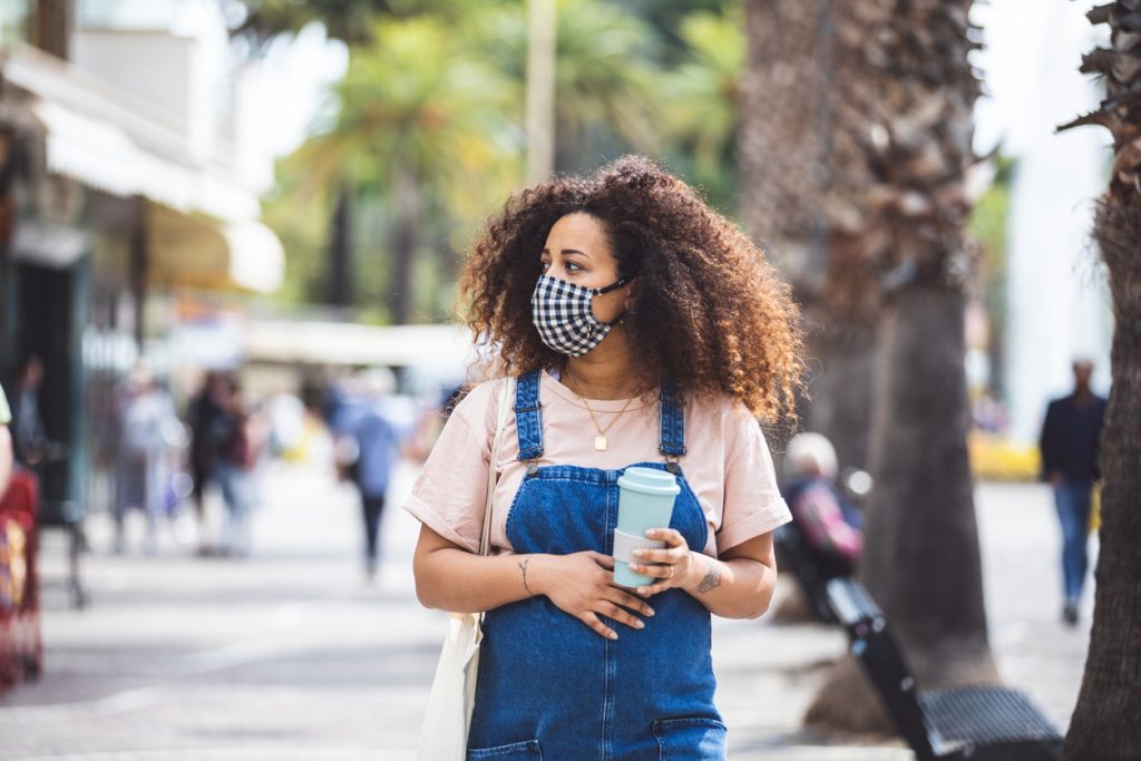 Pregnant woman walking in the city in a sunny day protecting herself with a cloth face mask
