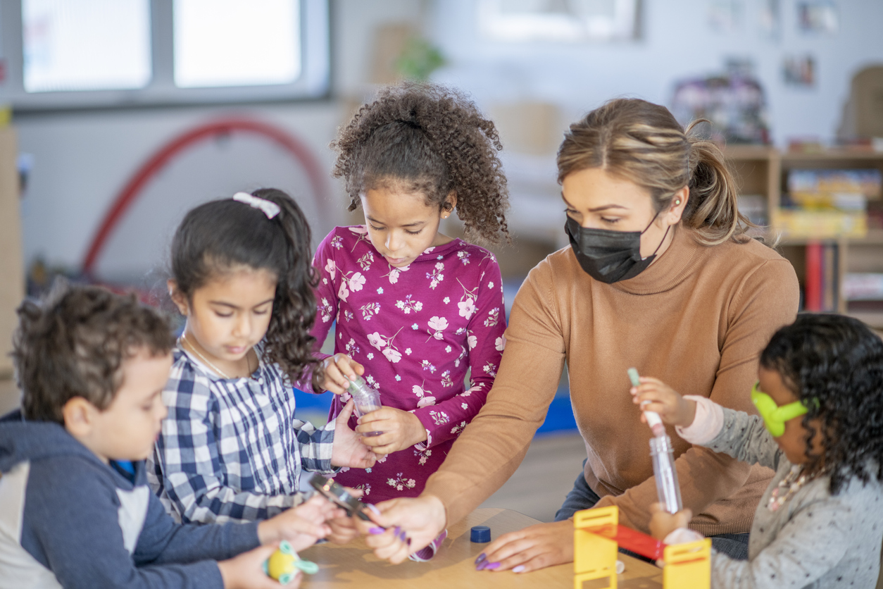 A teacher helps her diverse group of students build a structure with plastic pieces.