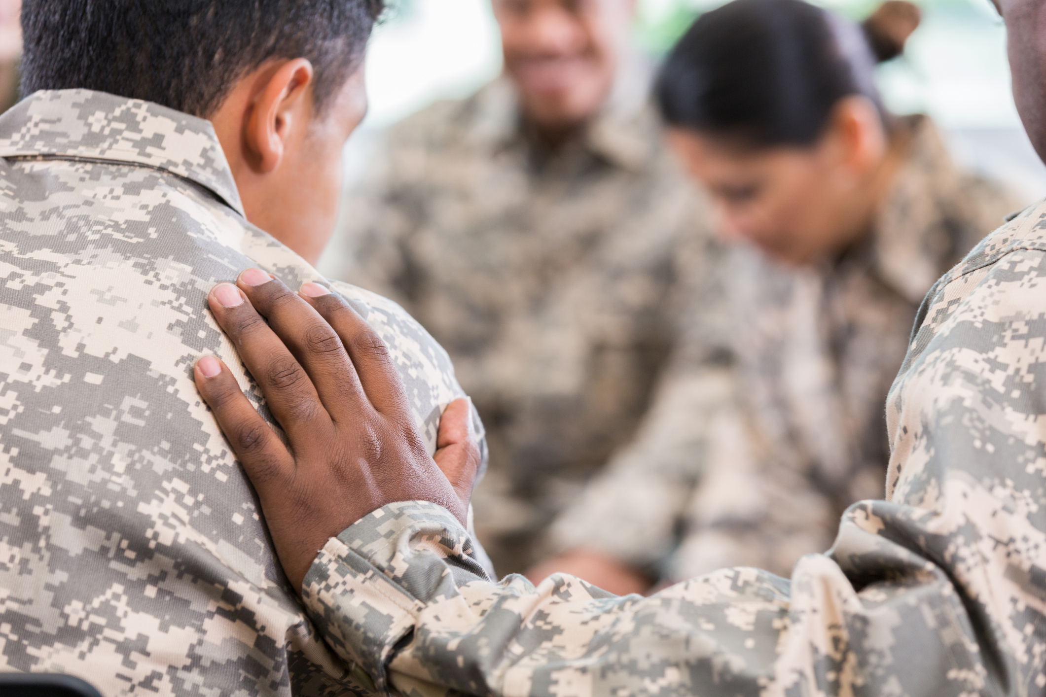 Unrecognizable soldier places his hand on fellow soldier while praying for him during a support group meeting.