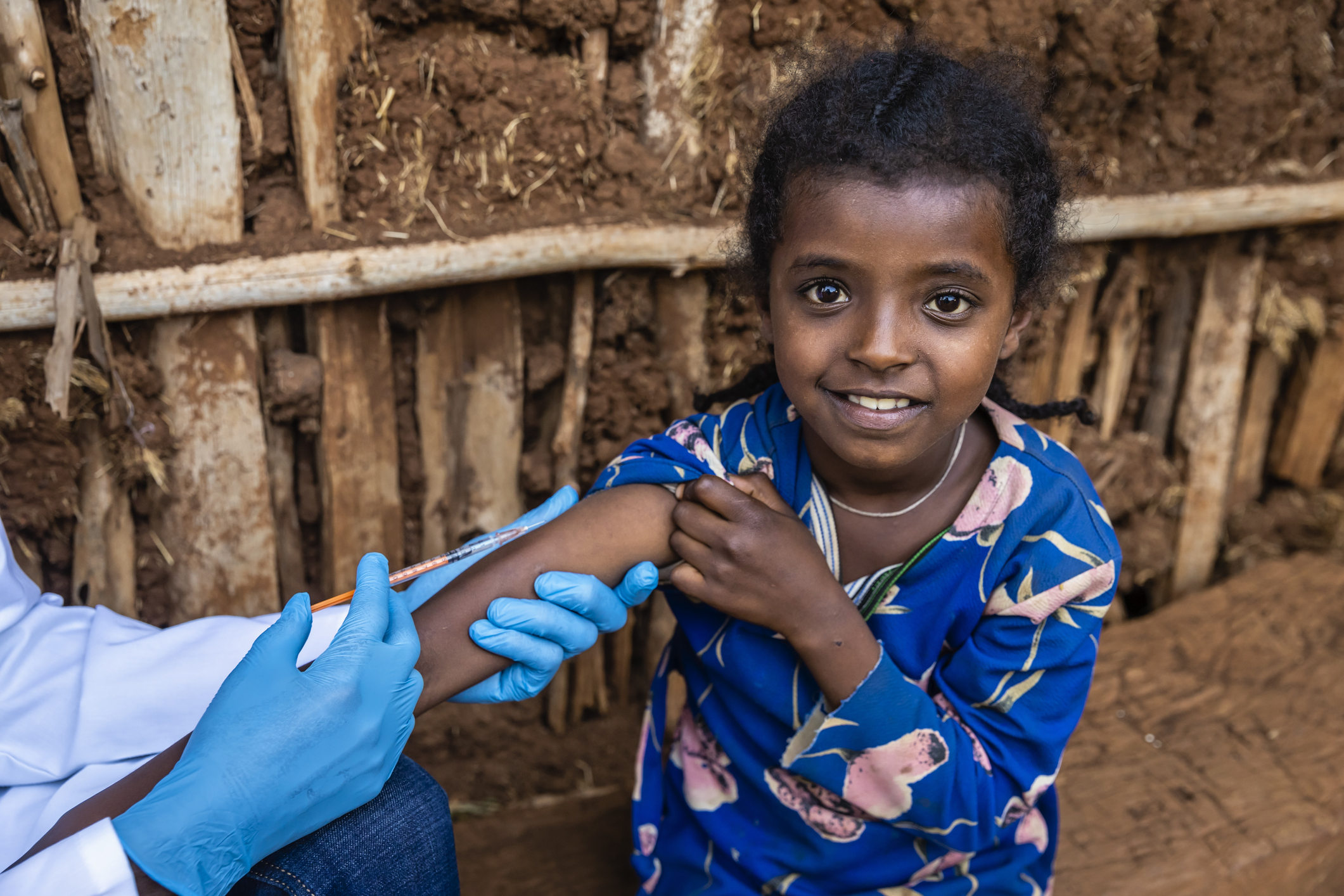 Male doctor vaccinating young African girl in small village, East Africa.