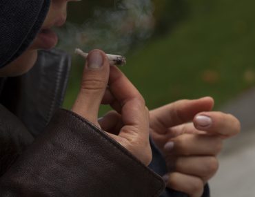 Young girl wearing leather jacket smoking a joint