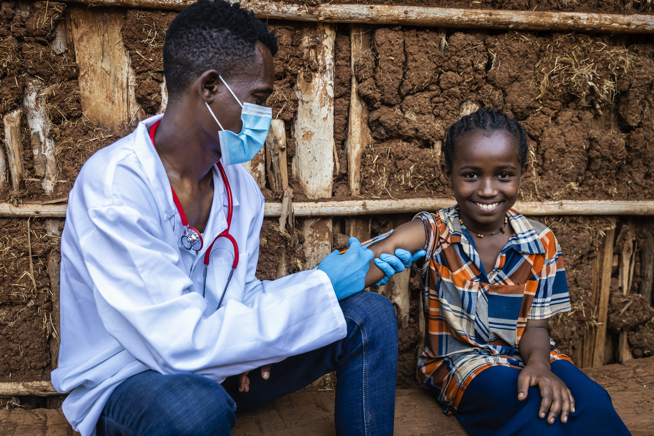 Male doctor vaccinating young African girl in small village, East Africa.