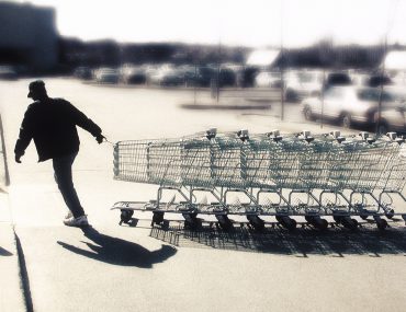 man gathering shopping carts in supermarket parking lot