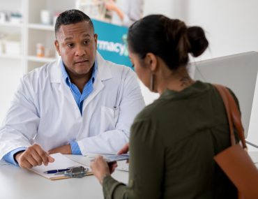 Female pharmacy customer asks a male pharmacist questions about a vaccine.