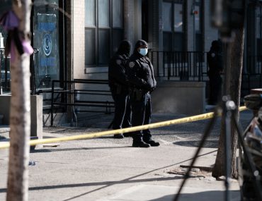 police officers wearing surgical masks stand in front of yellow tape