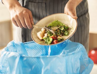 person scraping a plate of food into the trash
