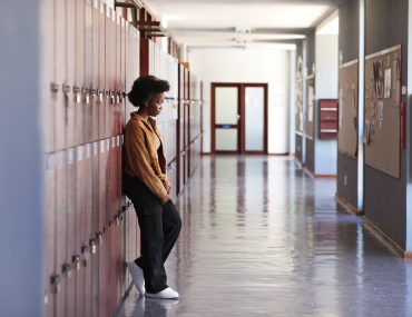 Sad teenage girl leaning on lockers in hallway