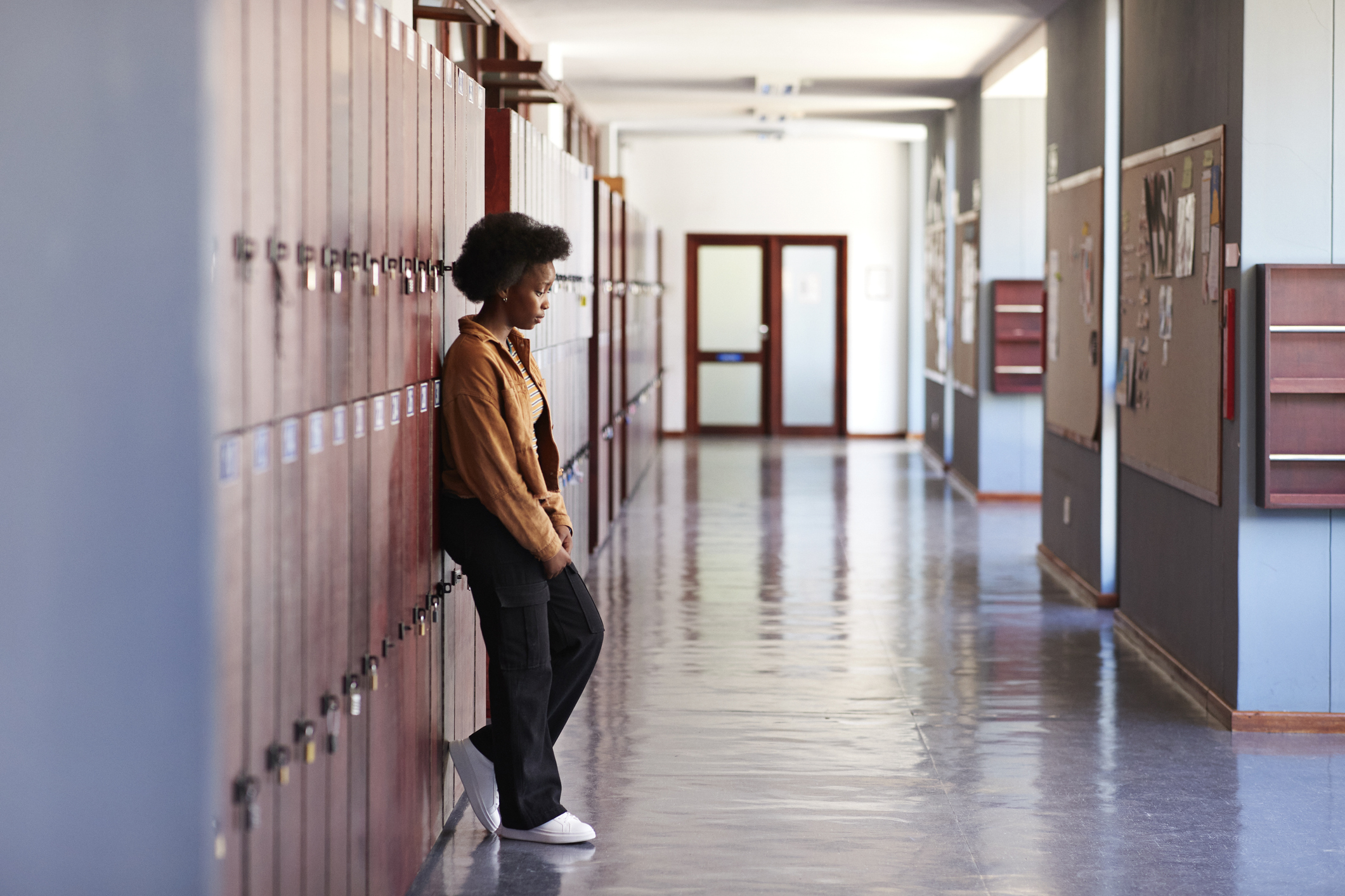 Sad teenage girl leaning on lockers in hallway