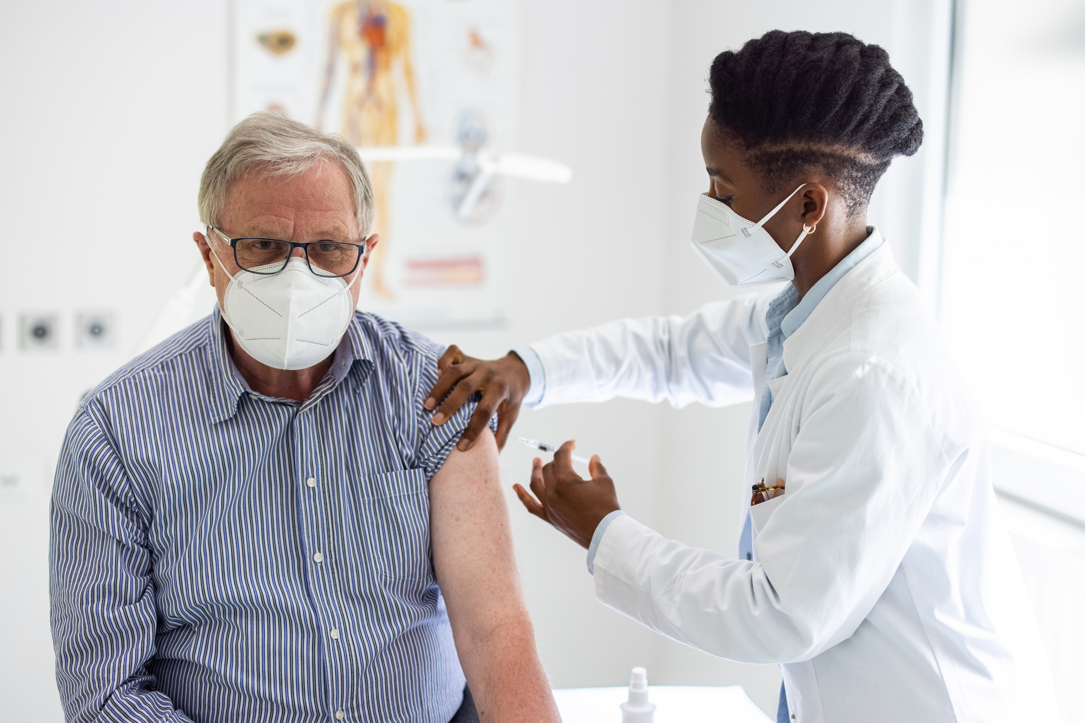 Female doctor giving a vaccine injection to a senior man in clinic during pandemic